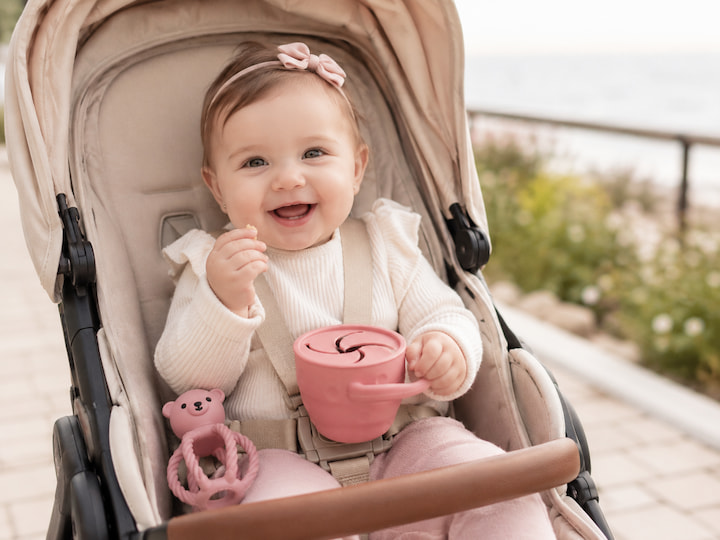 Bebeluș în cărucior, cu snack cup-ul și jucăria de dentiție din setul cadou Blupio Explorer Rose.